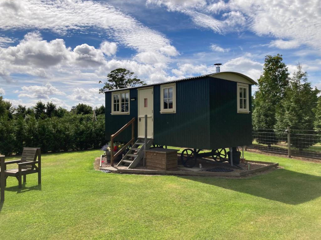 a green tiny house in a field with a bench at The Rowan Shepherds Hut in Eyemouth