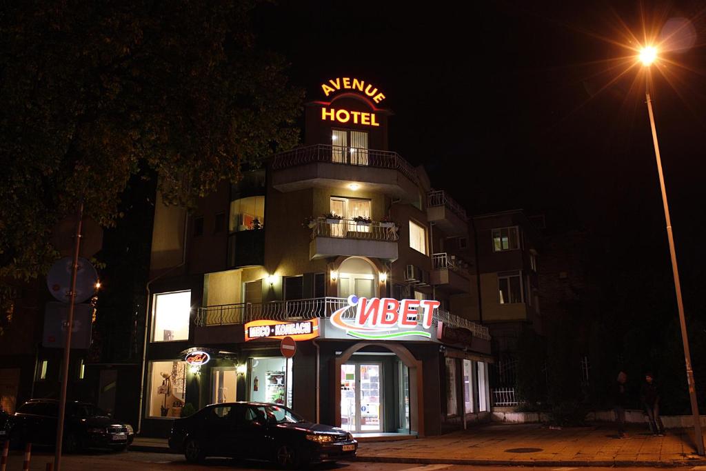 a hotel with a sign on top of it at night at Avenue in Shumen