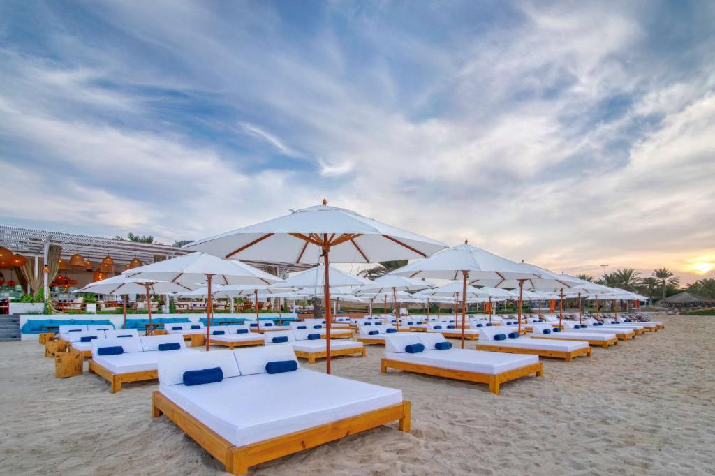a beach area with chairs, tables and umbrellas at Radisson Blu Hotel & Resort, Abu Dhabi Corniche in Abu Dhabi