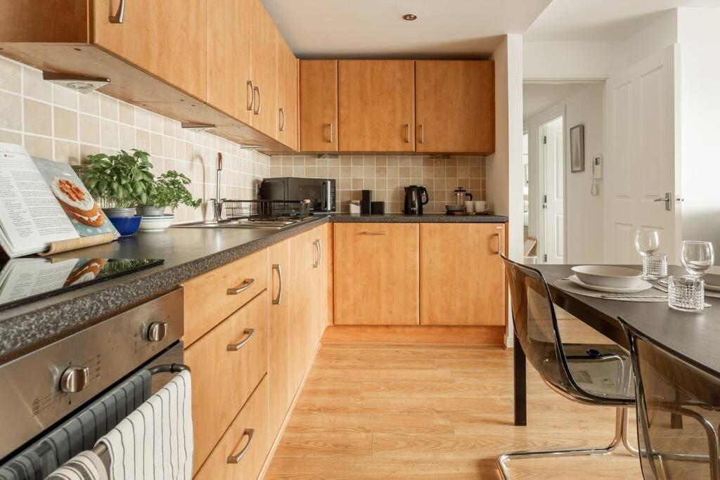 cocina con armarios de madera, mesa y encimera en Lux Waterfront 2 bed Apt, V&A 10min walk, St Andrew's Golf 25min drive en Dundee