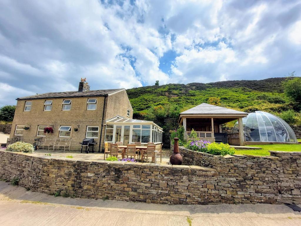 a house with a greenhouse next to a stone wall at Long Ing Farm in Holmfirth