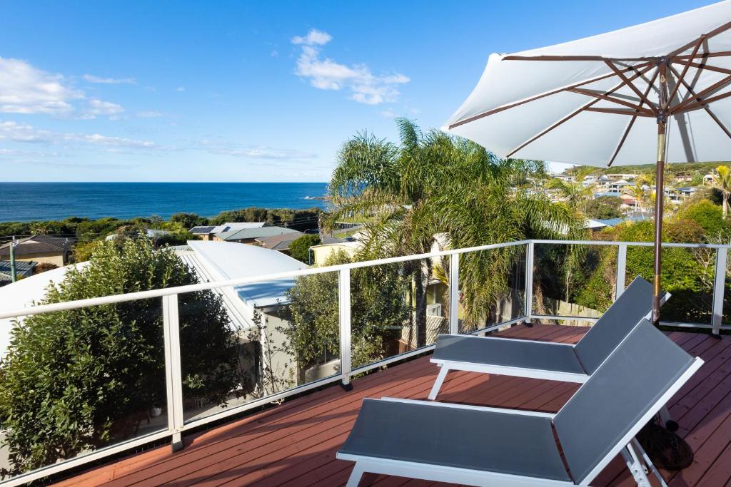 a deck with a chair and an umbrella and the ocean at Palm Road in Forster