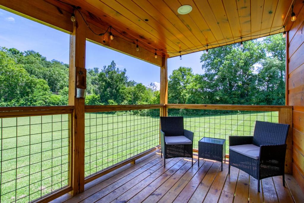 porche cubierto con sillas y vistas al bosque en Patriots Tiny Home w Hot Tub Fire Pit Grill en Sevierville