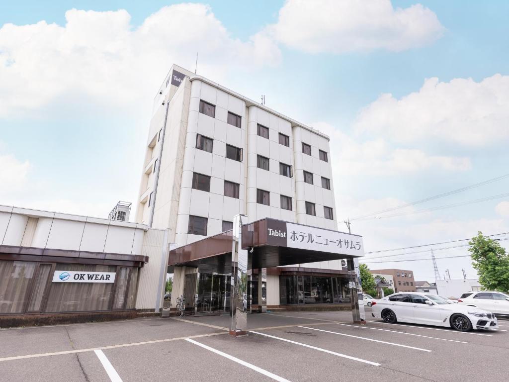 a white building with a car parked in a parking lot at Tabist Hotel New Osamura Sabae Inter in Fukui