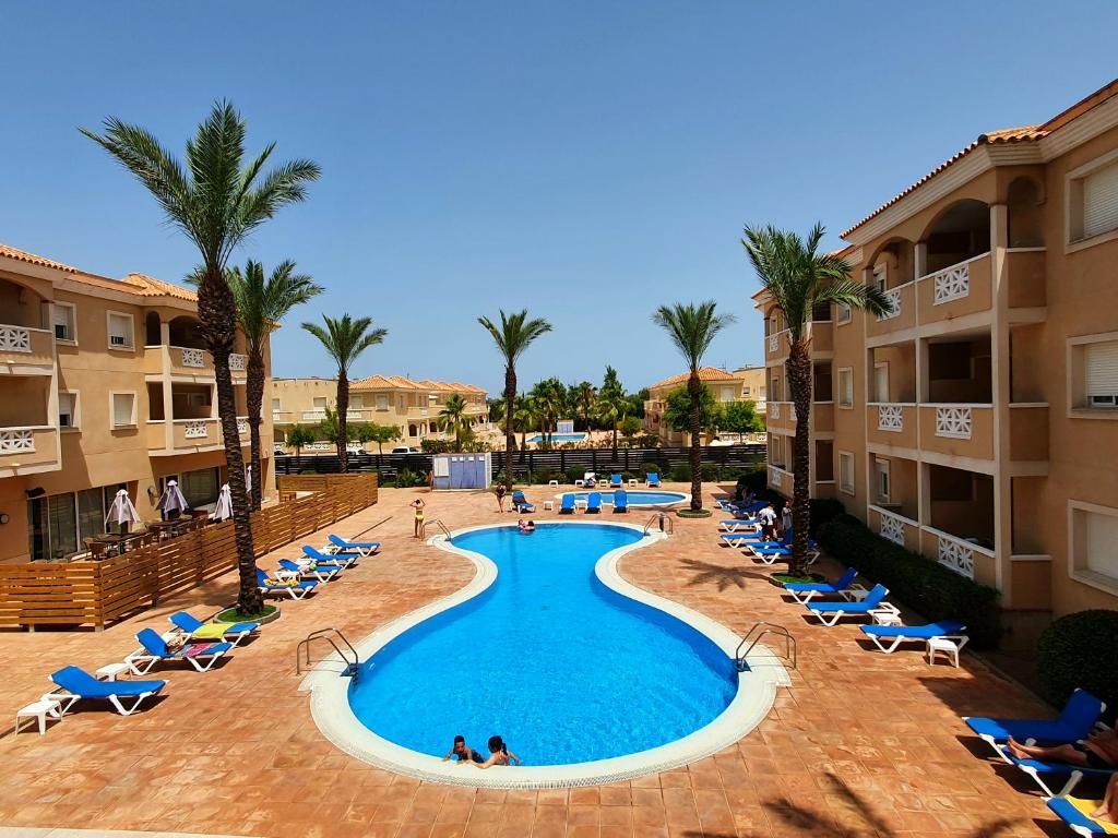 einen Pool in einem Resort mit Stühlen und Palmen in der Unterkunft Apartamentos Las Dunas-B in Riumar