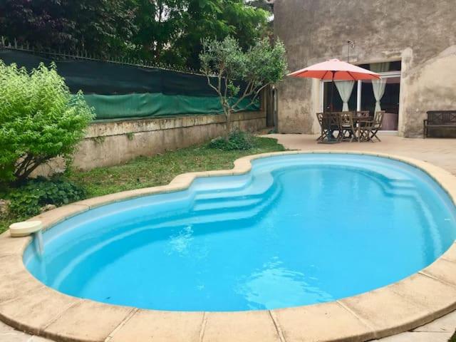 une grande piscine bleue avec une table et un parasol dans l'établissement Gîte Le Roucoul, à Maraussan