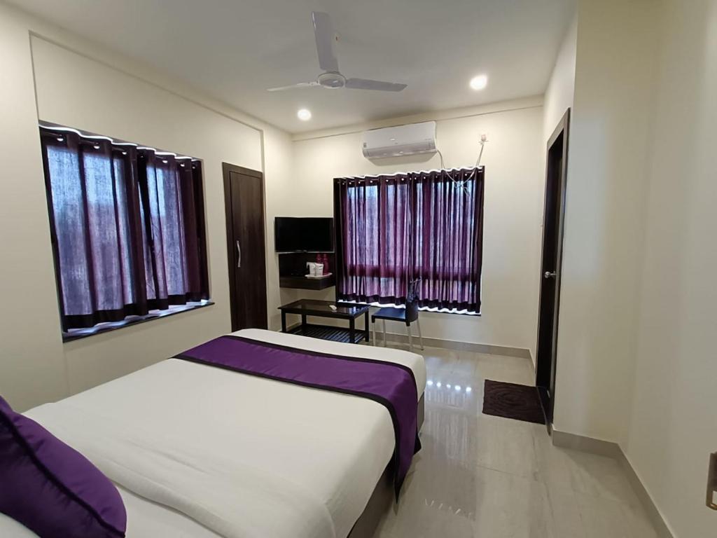 a bedroom with a bed and two windows and a table at Sheldon Inn Kolkata in Kolkata