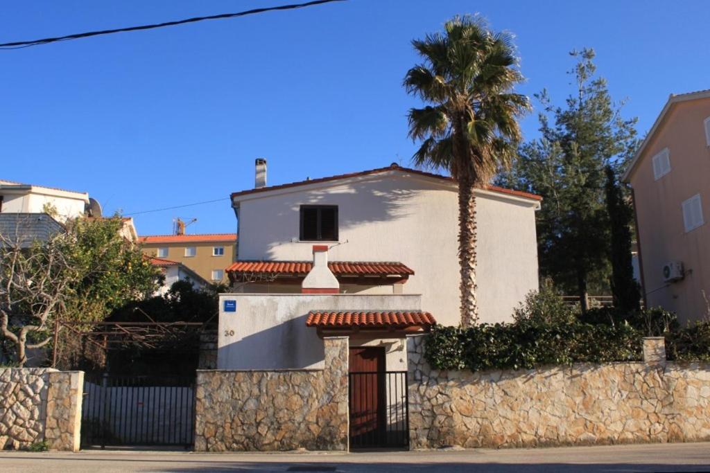a white house with a palm tree and a wall at Apartments with a parking space Seget Vranjica, Trogir - 8623 in Seget Vranjica
