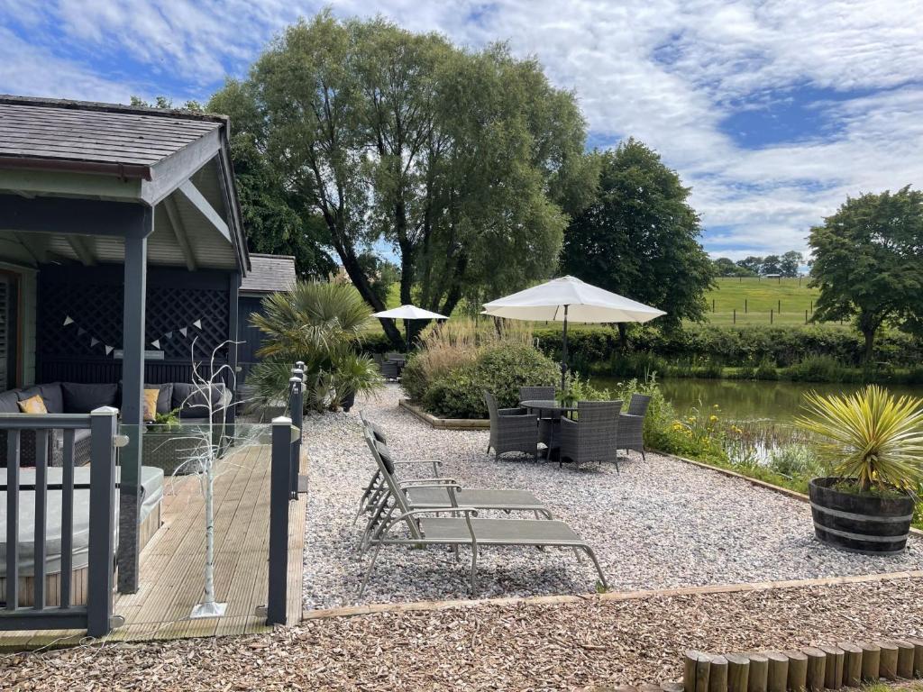 a patio with chairs and an umbrella next to a pond at Kingfisher Lodge, South View Lodges, Exeter in Exeter