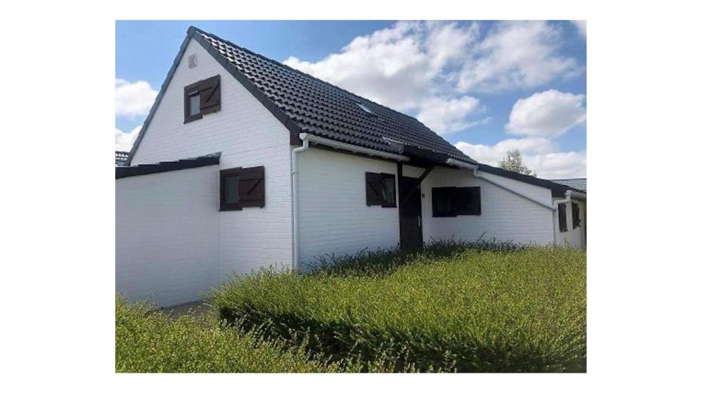 a white house with a black roof in a field at vakantiehuis 48 in Wenduine