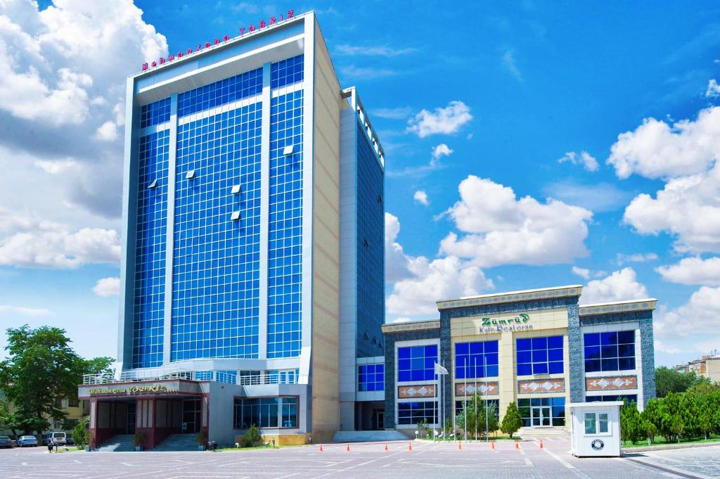 a large building with blue windows in a parking lot at Tebriz Hotel Nakhchivan in Naxçıvan