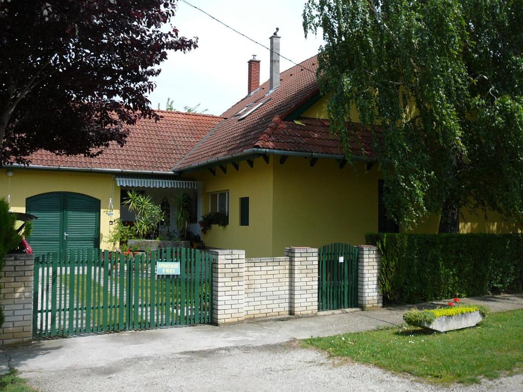uma casa amarela com uma cerca verde em frente em Tilesch Apartment em Balatonberény