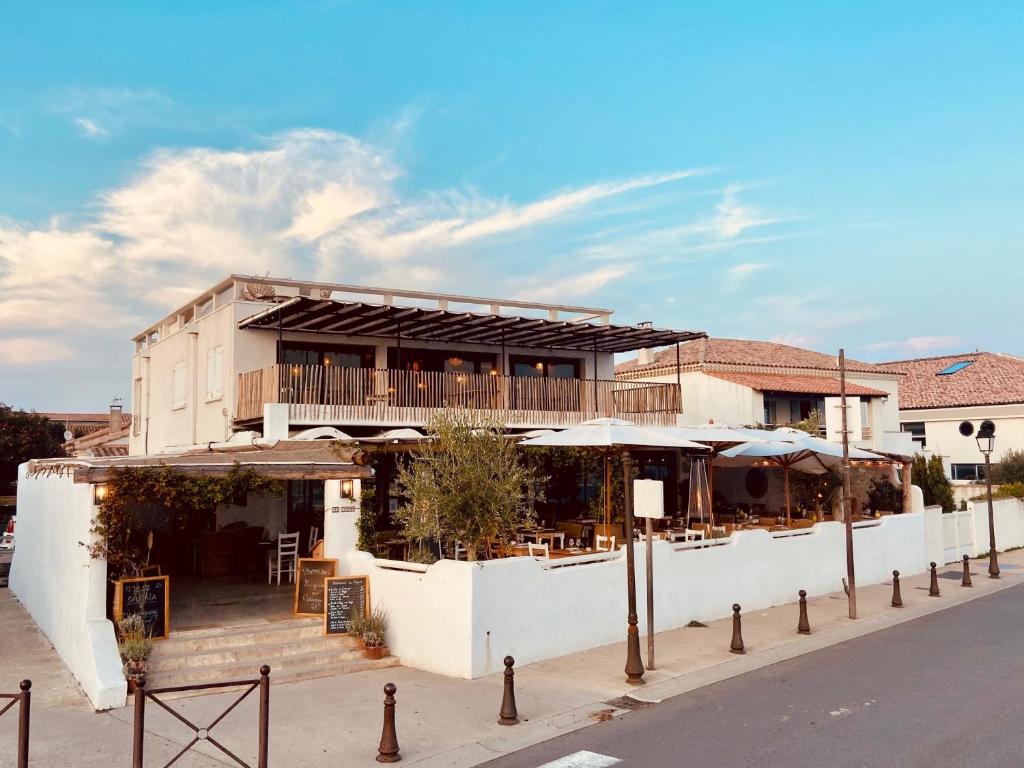 un edificio bianco con tavoli e ombrelloni su una strada di Les Vagues a Saintes-Maries-de-la-Mer