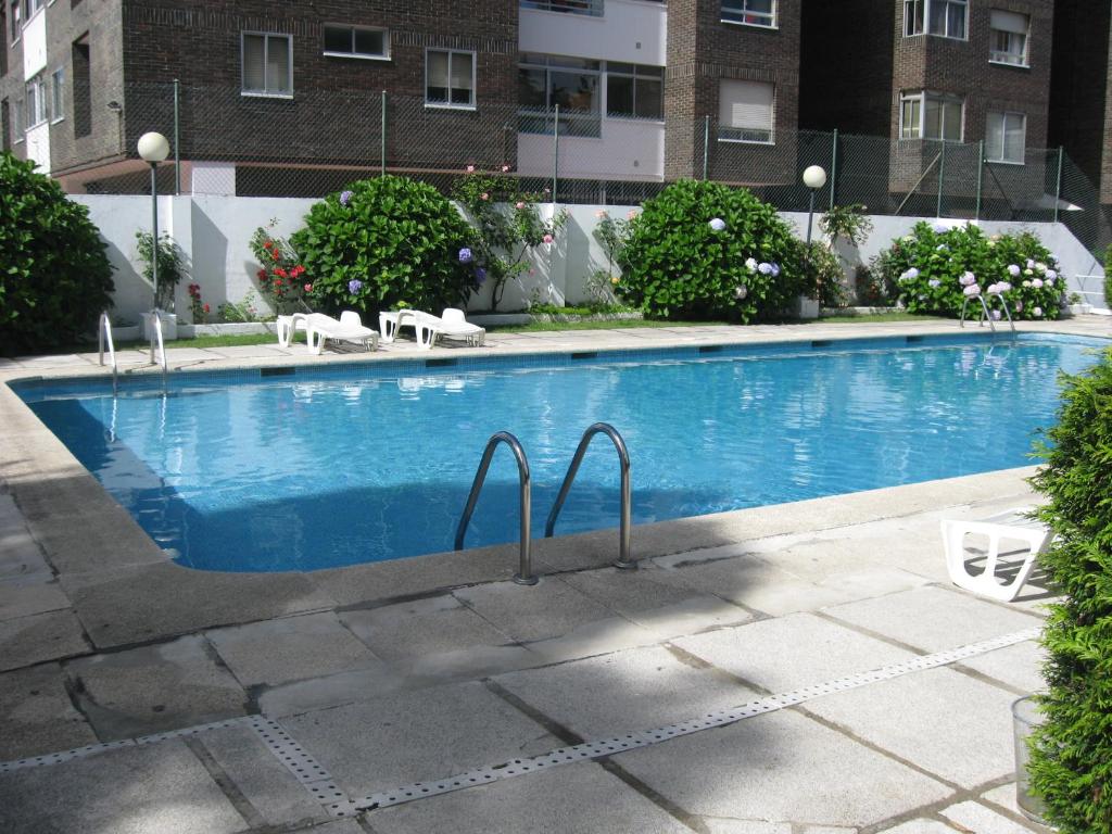 a swimming pool with two chairs and a building at Apartamento Bamuxela in Vigo