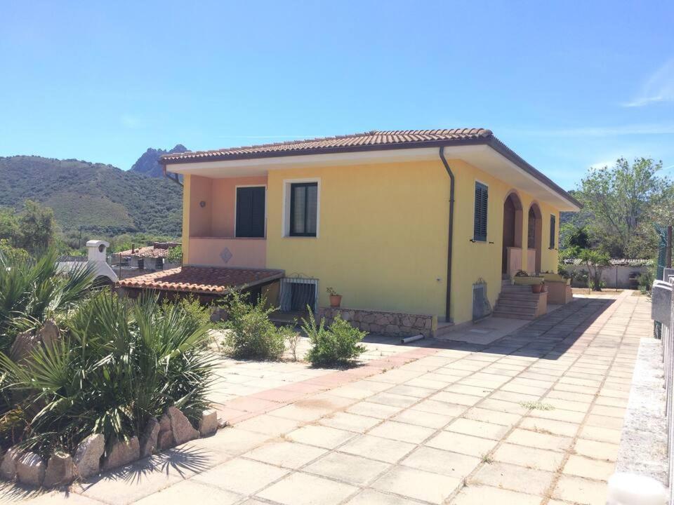 uma pequena casa amarela com montanhas ao fundo em Casa Piana em Viddalba