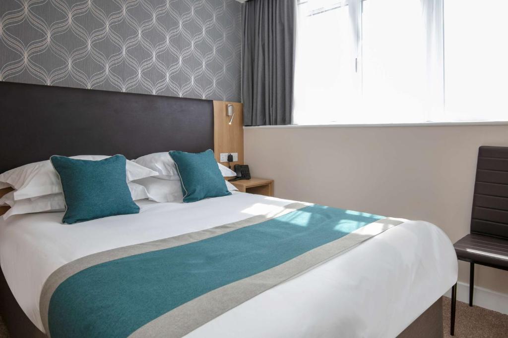 1 dormitorio con 1 cama grande con almohadas azules en Best Western Northfields Ealing Hotel, en Londres