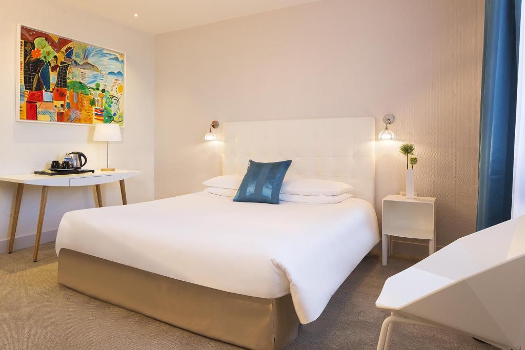 a bedroom with a large white bed with a blue pillow at Hôtel Escale Oceania Lorient in Lorient