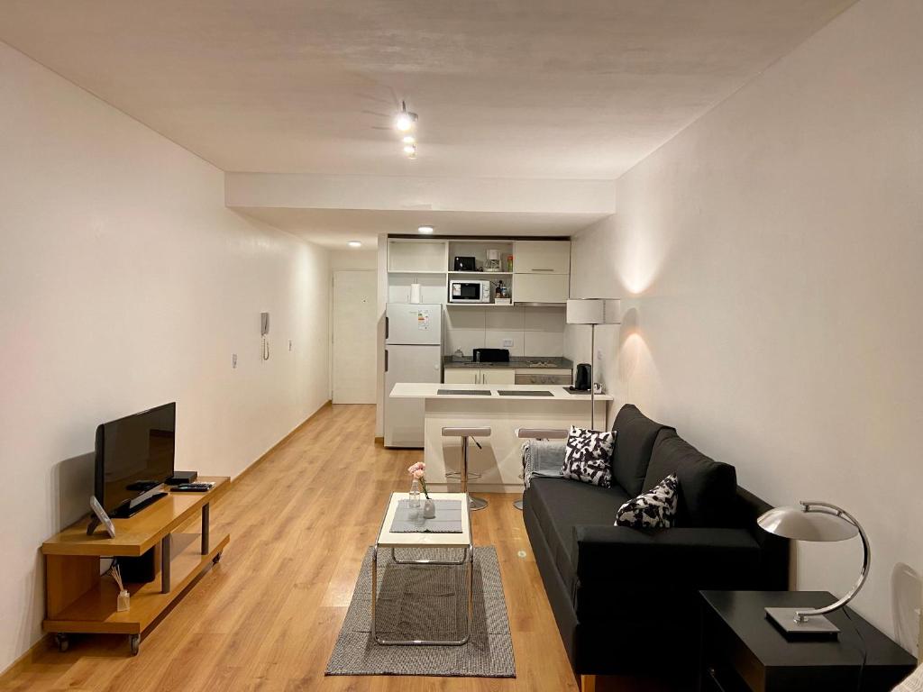 ein Wohnzimmer mit einem schwarzen Sofa und einem TV in der Unterkunft Apartamento Céntrico y Moderno con Balcon, Piscina, Gimnasio y Laundry in Buenos Aires