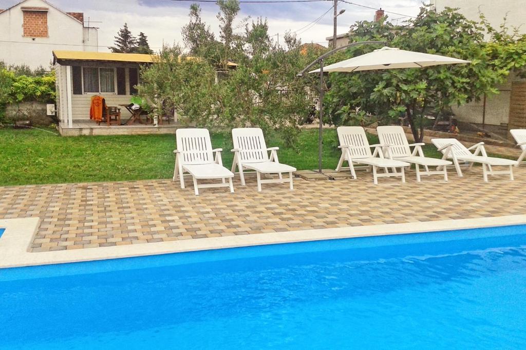 eine Gruppe Stühle und ein Sonnenschirm neben einem Pool in der Unterkunft Family friendly apartments with a swimming pool Biograd na Moru, Biograd - 8371 in Biograd na Moru