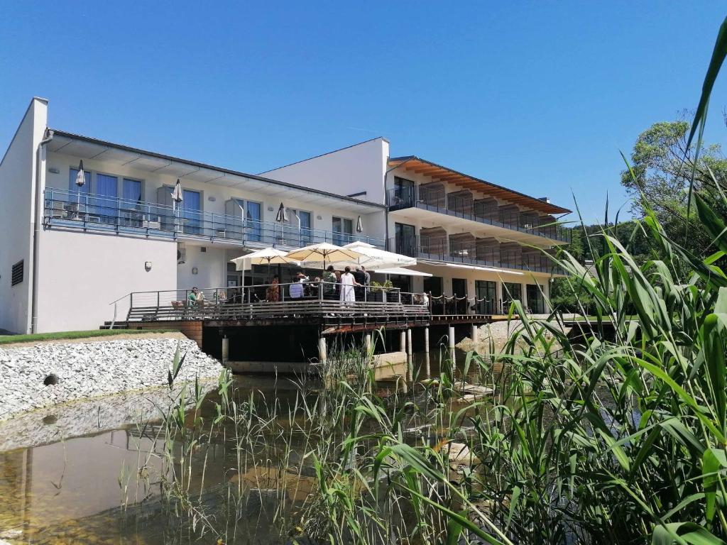 a building with tables and umbrellas next to a body of water at Green Business Hotel am Mühlengrund Graz in Graz