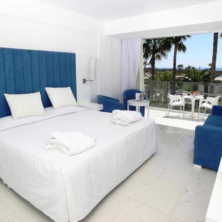 biała sypialnia z dużym białym łóżkiem i niebieskimi krzesłami w obiekcie Dome Beach Marina Hotel & Resort w Ajia Napa