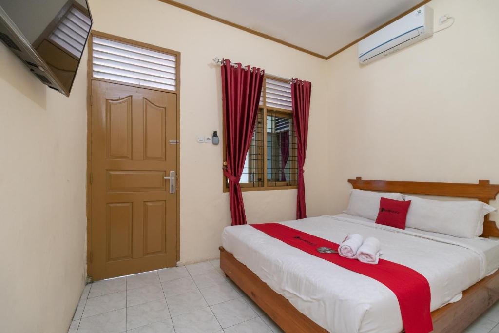 a bedroom with a bed with red curtains and a door at RedDoorz near RS Awal Bros Sudirman Pekanbaru in Parit