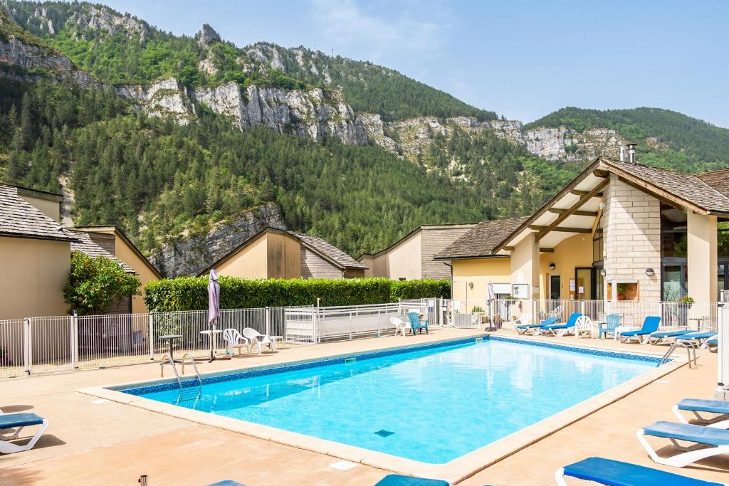 uma piscina num hotel com montanhas ao fundo em Village de gîtes de Blajoux em Quézac