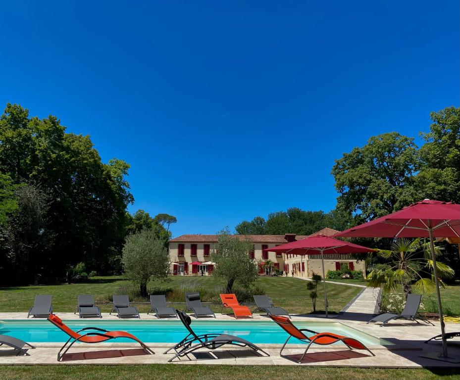 a pool with chairs and umbrellas in front of a building at Maison D'hôtes Sainte-Marie in Mirande