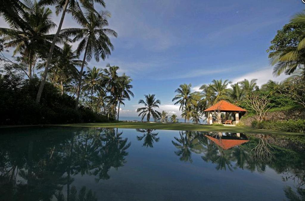 a pool of water with a gazebo and palm trees at Villa Rumah Pantai Bali in Selemadeg