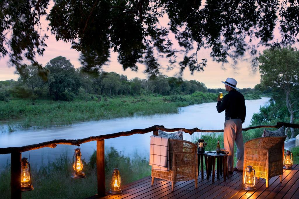 a man standing on a deck next to a river at Lion Sands - Tinga Lodge in Skukuza