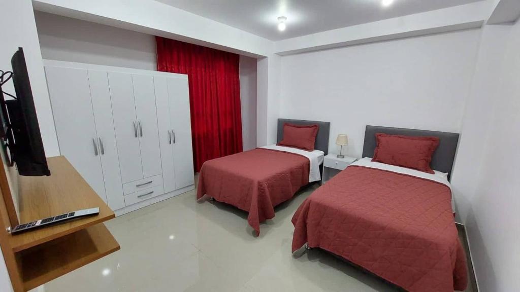 a bedroom with two beds with red sheets and a tv at Departamentos amoblados en Huánuco in Huánuco