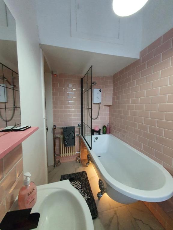 eine große weiße Badewanne im Bad mit rosa Fliesen in der Unterkunft The Flat with the Pink Door in Edinburgh