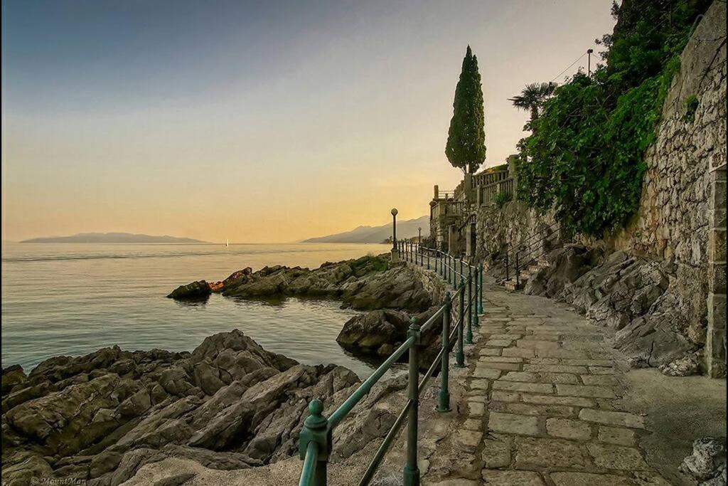 a stone path next to the water with a tree at Apartments Villa Dinka in Opatija