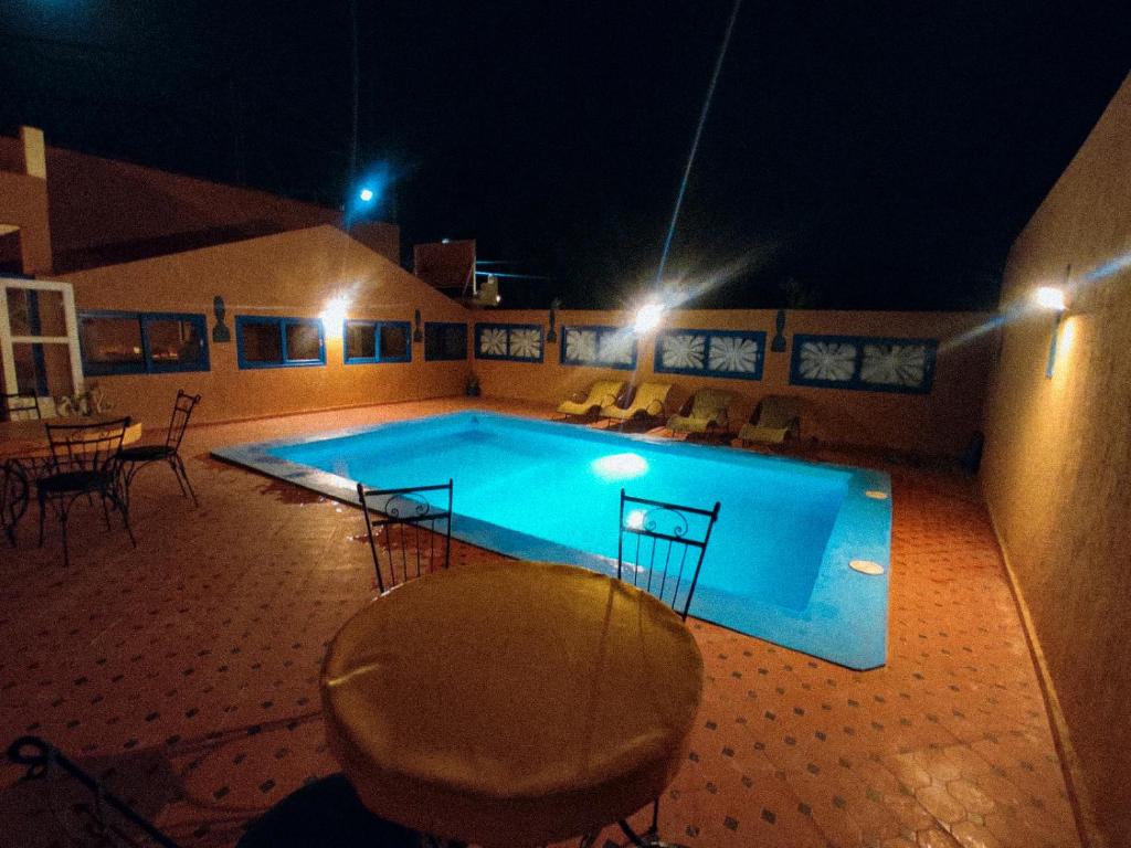 a swimming pool at night with a table and chairs at La Baraka Auberge in Aït Benhaddou