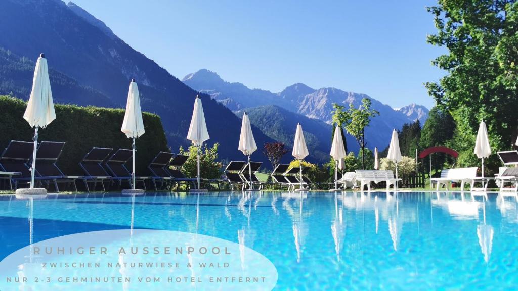 una piscina con sombrillas blancas y una montaña en Vital- & Familienhotel Angerwirt en Kleinarl