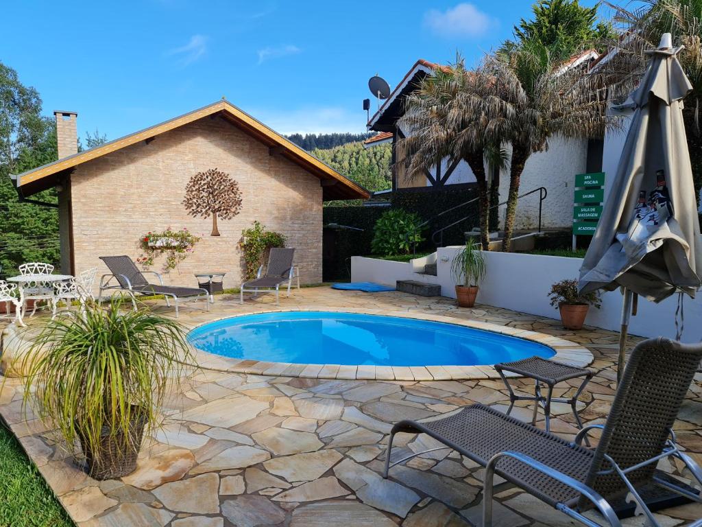 una piscina en un patio con sillas y sombrilla en Chalés Valle Florido, en Monte Verde