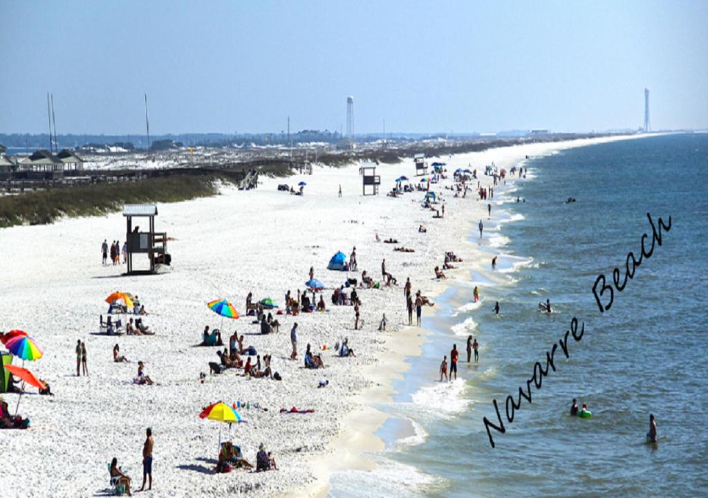 a crowd of people on a beach with a sign that reads vacation at Navarre Beach Escapades-Pet Friendly in Navarre