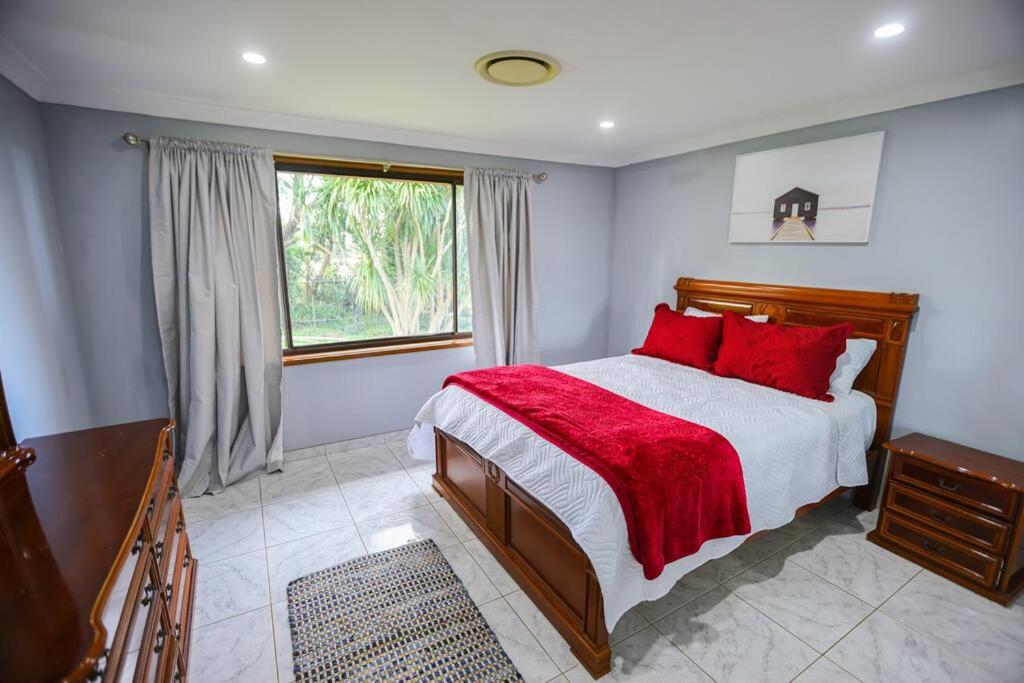 a bedroom with a bed with red pillows and a window at Entire House Beautiful Farm Stay 9 Bedrooms Sleeps 18 Enjoy Nature in Mangrove Mountain