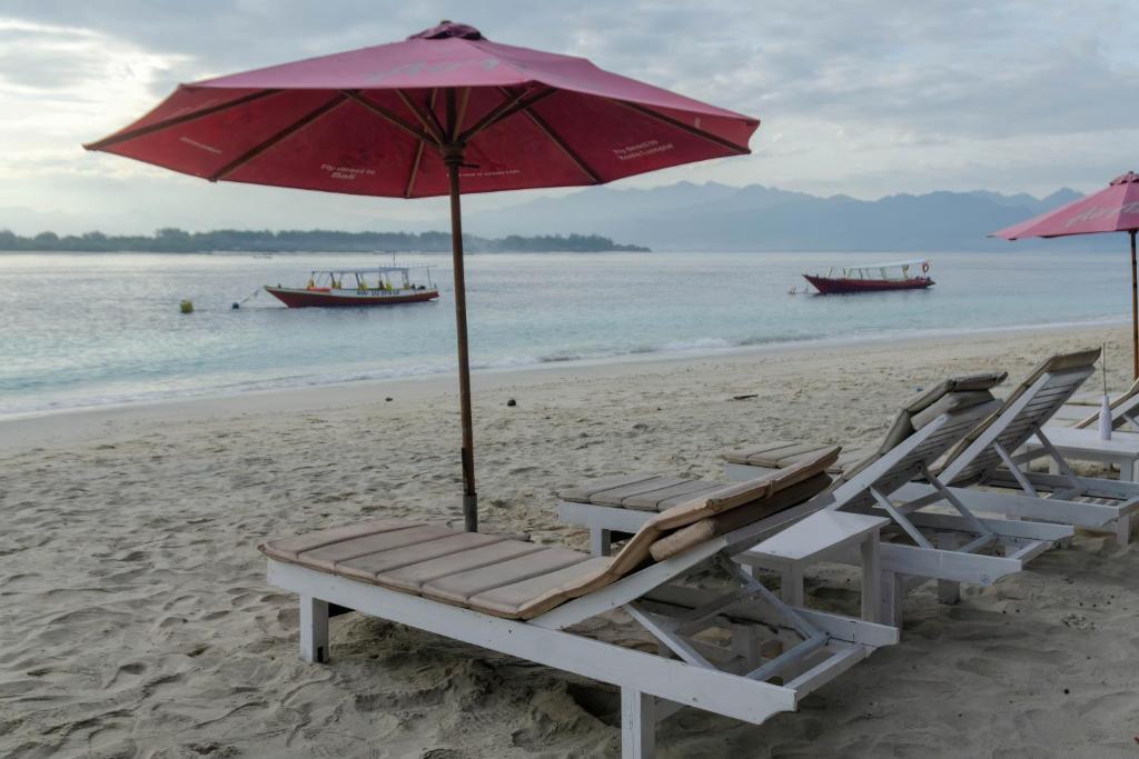 two lounge chairs and an umbrella on a beach at Warna Beach Hotel in Gili Trawangan