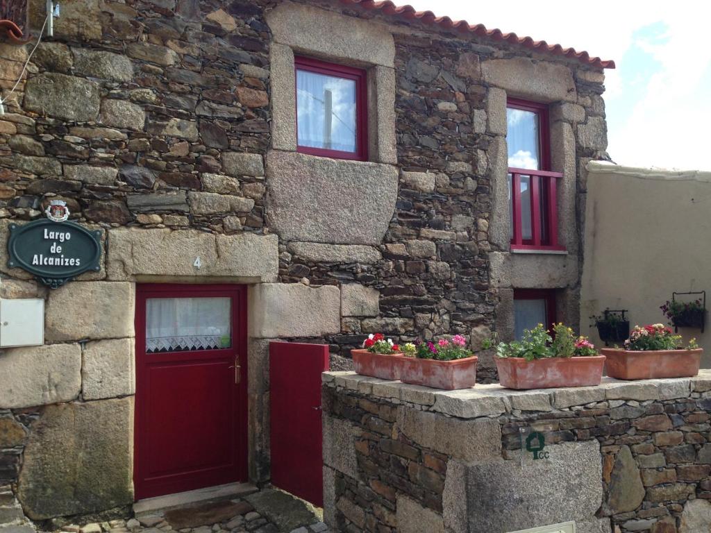 un edificio de piedra con puertas rojas y macetas en Palheiro do Castelo - Pátio, en Sabugal
