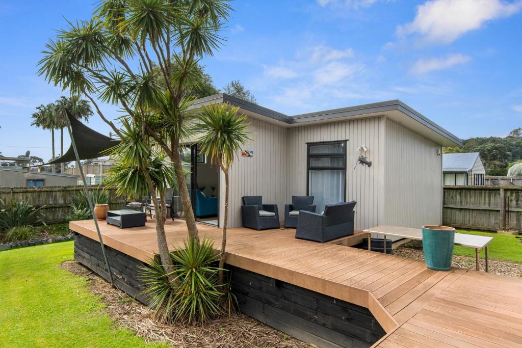 a deck with chairs and a table and palm trees at Bayside Beauty - Matapouri Holiday Home in Matapouri