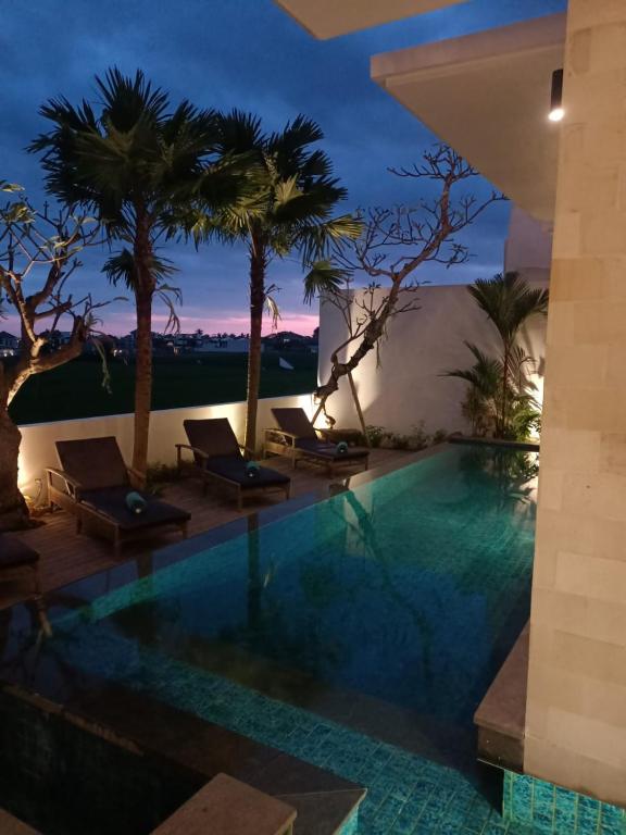 a pool at night with palm trees and chairs at The Kd Suites & Coffee Shop in Munggu