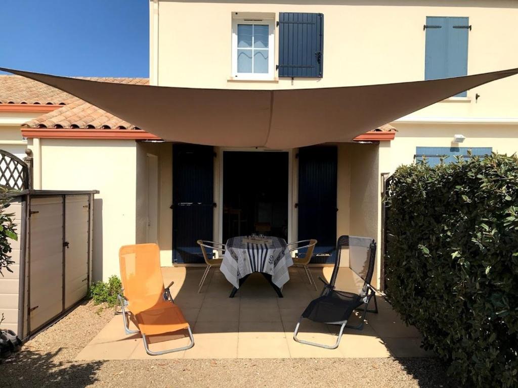 un patio avec une table et des chaises devant une maison dans l'établissement Maison 3 pièces près de la plage avec piscine, terrasse, et parking à Bretignolles-sur-Mer. - FR-1-224A-17, à Bretignolles-sur-Mer