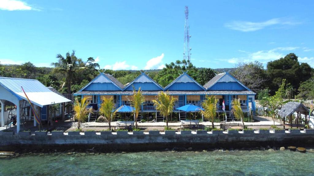 un edificio blu con palme di fronte all'acqua di Moyo Island Resort a Moyo Island