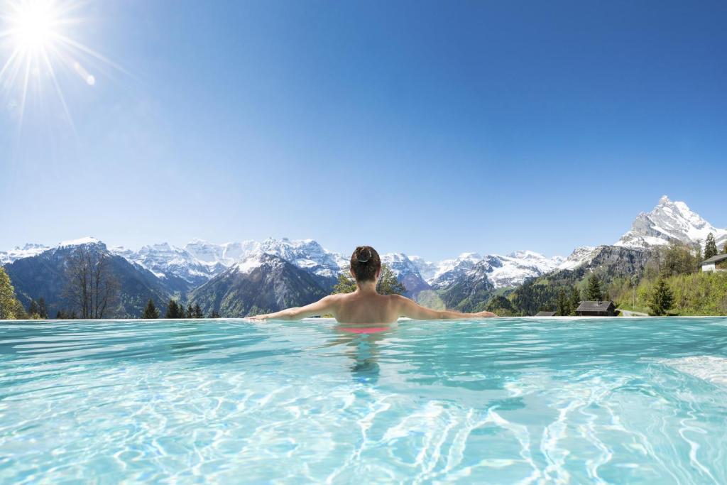 un hombre en una piscina infinita con montañas en el fondo en Märchenhotel, en Braunwald