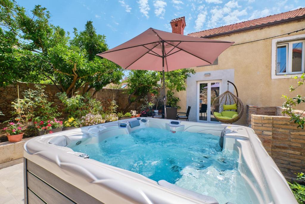 a hot tub with an umbrella in a backyard at SkyGarden House in Mali Lošinj