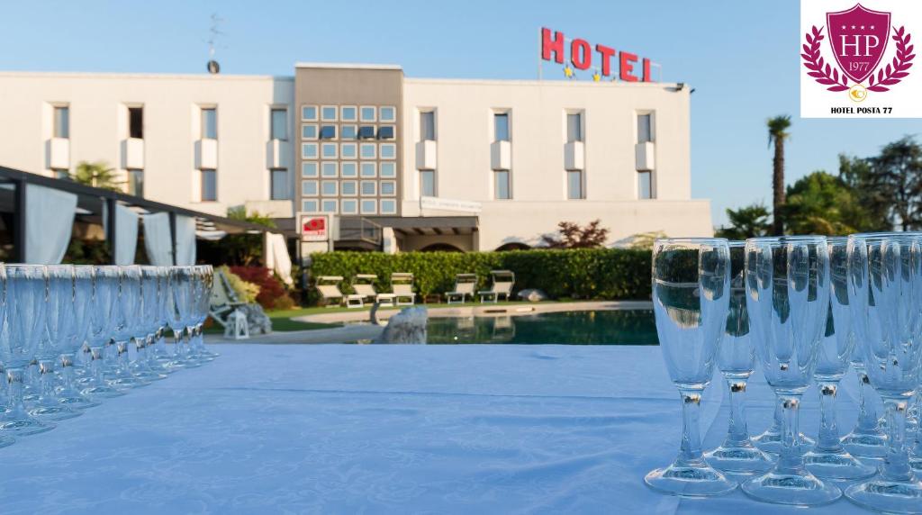 uma fila de copos de vinho sentados numa mesa em frente a um hotel em Hotel Posta 77 em San Giorgio in Bosco