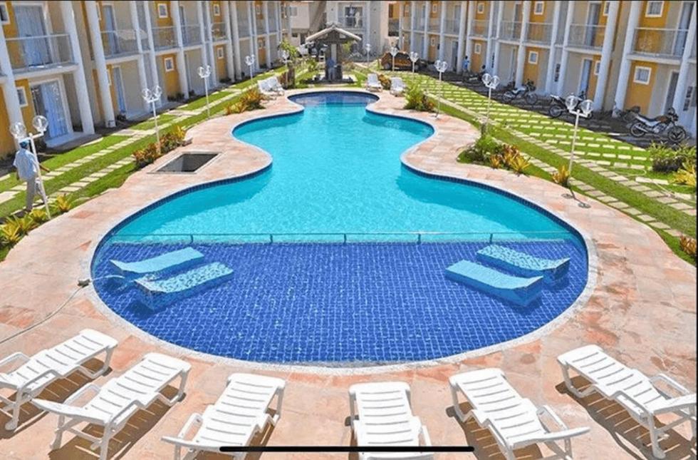 una grande piscina con sedie a sdraio e un resort di DUPLEX 2 SUÍTES CONDOMÍNIO MONT CARMELO a Porto Seguro
