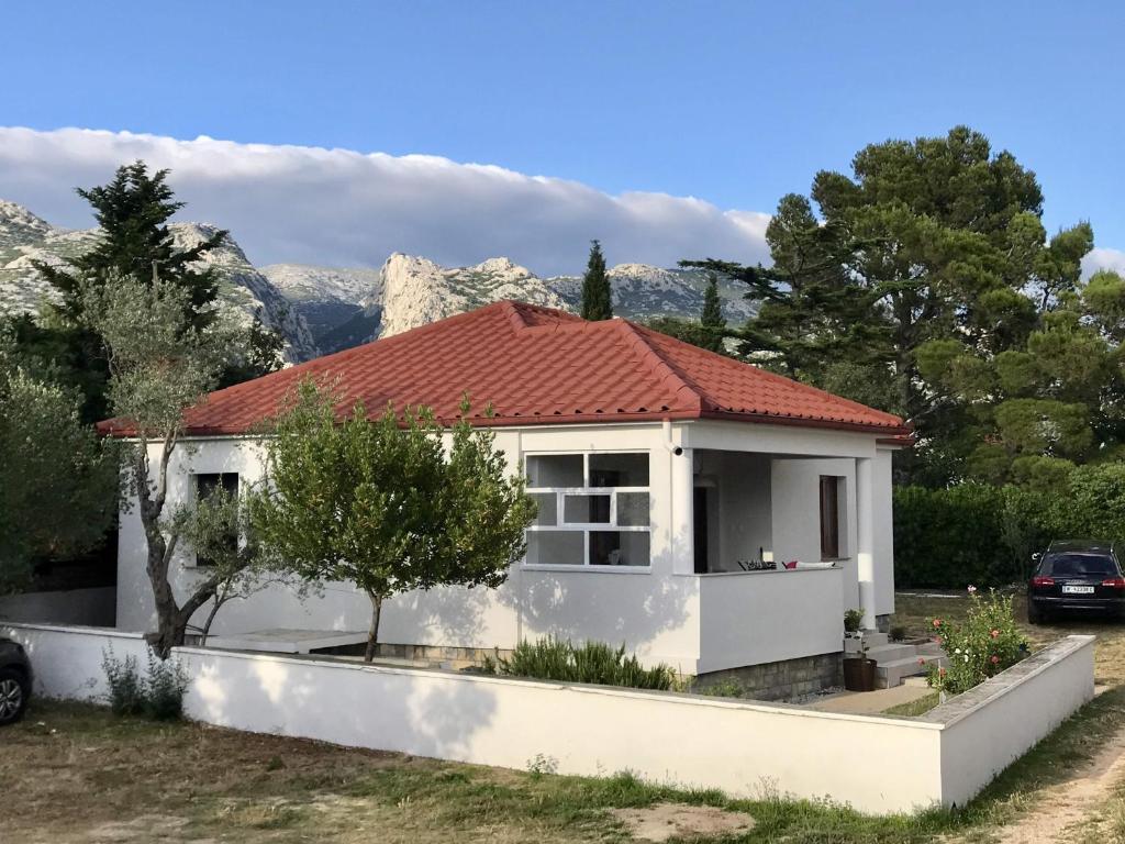 uma casa branca com um telhado vermelho com montanhas ao fundo em Holiday house with a parking space Seline, Paklenica - 16318 em Starigrad-Paklenica