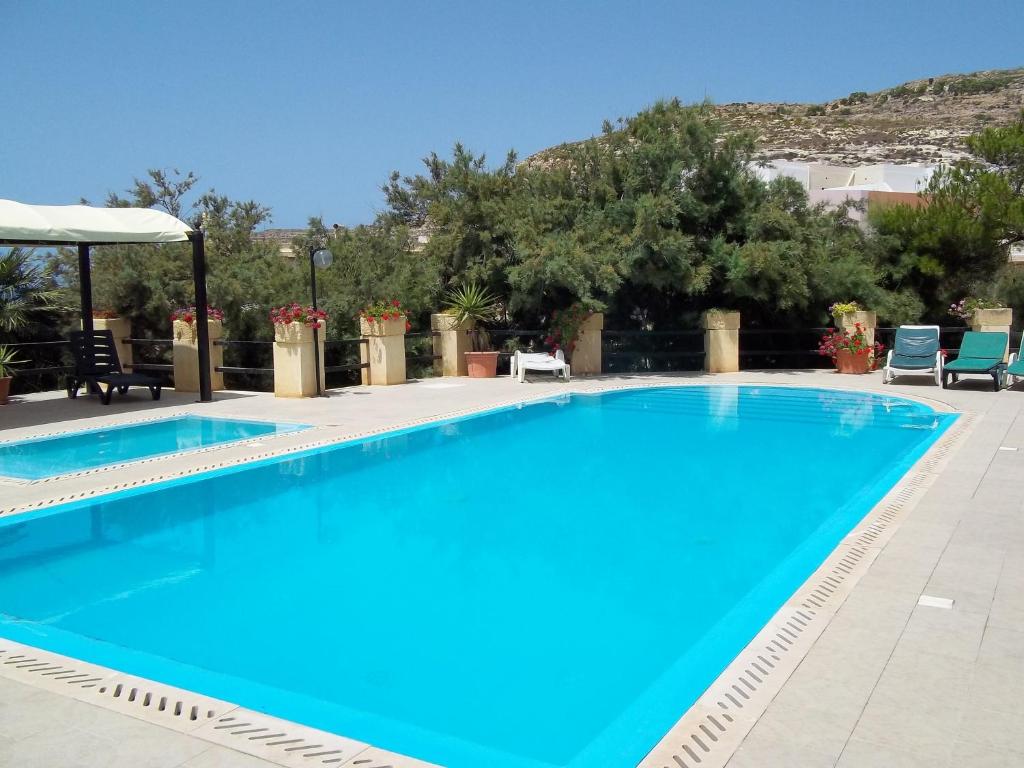 a large blue swimming pool with chairs and trees at San Antonio Guesthouse in Xlendi